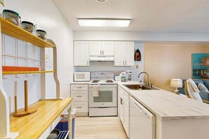 A compact kitchen with white cabinets, a microwave, a stove, and a sink.