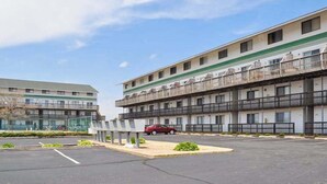 Ein mehrstöckiges Motel mit Balkonen, einem Parkplatz und einem roten Auto davor.