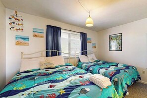 A bedroom with two beds, a window with curtains, and wall art.