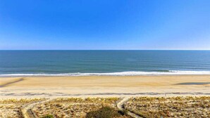 Une plage avec un ciel dégagé, un rivage sablonneux et un sentier menant à l’eau.