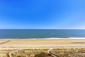 Ein Strand mit blauem Himmel, sandigem Ufer und einem Weg zum Wasser.