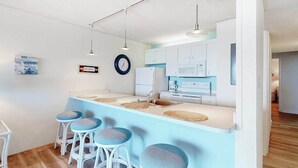 Une cuisine moderne avec des meubles blancs, un plan de travail bleu et quatre tabourets de bar.
