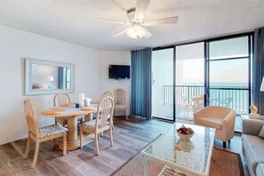 Ein Hotelzimmer mit Essbereich, einem Balkon mit Blick, einem Deckenventilator und einem Flachbildfernseher.