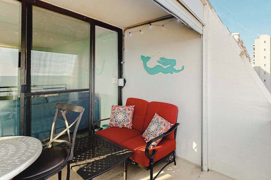 A balcony with a red sofa, a metal table, and a chair.