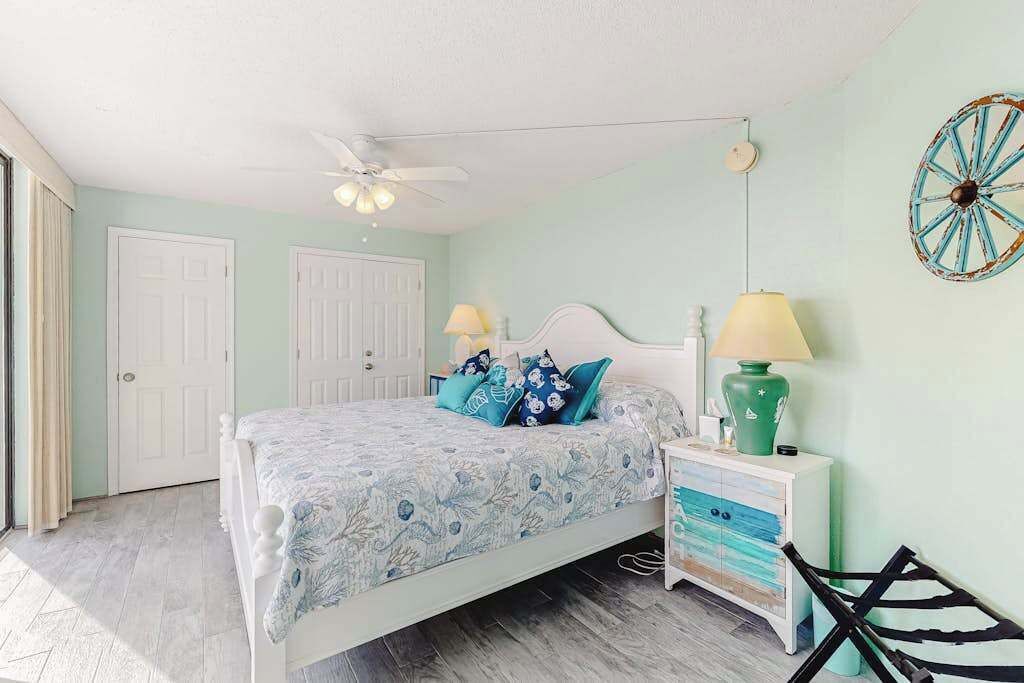 A bedroom with a bed, bedside tables, a ceiling fan, and a wall decoration.