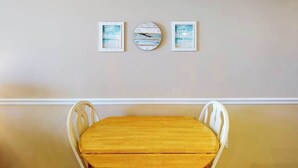 A dining area with a wooden table and white chairs, framed artwork on the wall, and a clock. - Polynesian 309 (Ocean City)