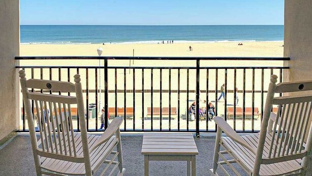A balcony with two white chairs and a small table, overlooking a beach with people and a clear sky. - Polynesian 309 (Ocean City)