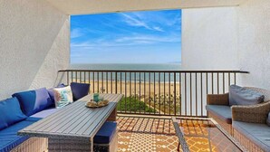 Een balkon met uitzicht op het strand, een tafel met kussens en een rieten zitzofa.