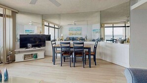 Een moderne woonkamer met een televisie, een eettafel, stoelen en een plafondventilator.