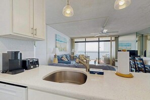 A modern kitchen with a built-in sink, a coffee maker, and a dining area with a table and chairs. - Bright, oceanfront condo with balcony, AC, laundry & outdoor pool (Ocean City)