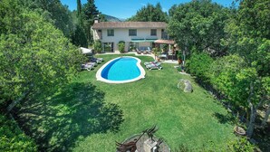 Uma casa com piscina, rodeada por um gramado bem cuidado e árvores.