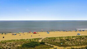 A beach with tents and umbrellas, a clear sky, and a calm sea. - Oceanfront Condo with a Balcony, Great View, AC, WiFi & Shared Outdoor Pool (Ocean City)