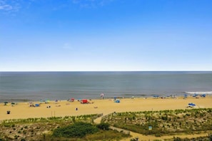 A beach with tents and umbrellas, a clear sky, and a calm sea. - Oceanfront Condo with a Balcony, Great View, AC, WiFi & Shared Outdoor Pool (Ocean City)
