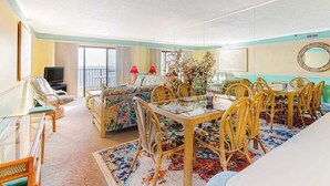 Une pièce comprenant une table à manger, des chaises, un canapé, un téléviseur et un balcon.