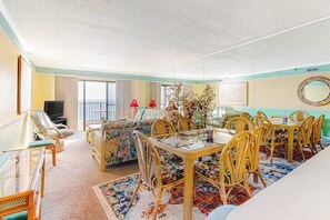 Ein Zimmer mit Esstisch, Stühlen, einer Couch, einem Fernseher und einem Balkon.