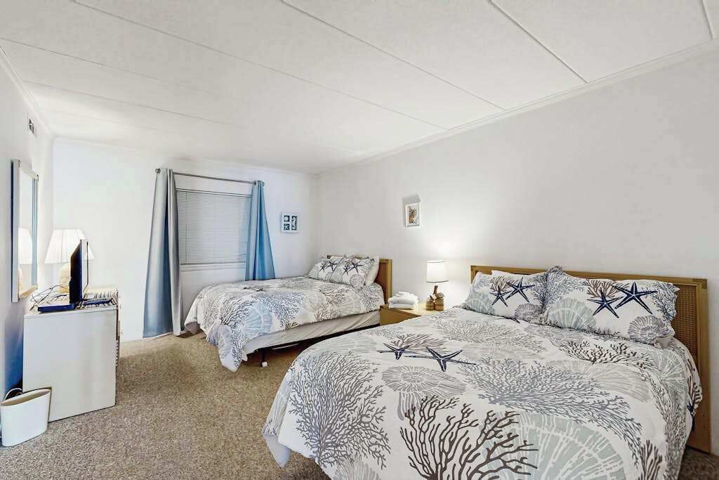 Una habitación de hotel con dos camas, un escritorio, una lámpara y una ventana con cortinas.