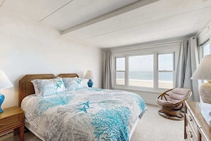 A bedroom with a bed, a window with curtains, a wicker chair, and a lamp. - Purnell House 402 (Ocean City)