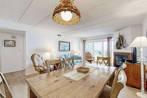 A dining area with a wooden table, chairs, a chandelier, and a television. - Purnell House 402 (Ocean City)