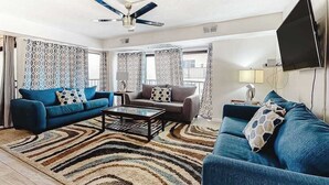 A living room with two sofas, a coffee table, a ceiling fan, and a TV. - Ocean Block Condo with Balcony, Partial Ocean View, Central AC & Washer/Dryer (Ocean City)