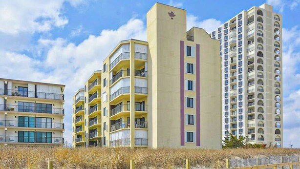 A beachfront hotel with multiple-story buildings, balconies, and a sandy beach area. - Ocean Block Condo with Balcony, Partial Ocean View, Central AC & Washer/Dryer (Ocean City)