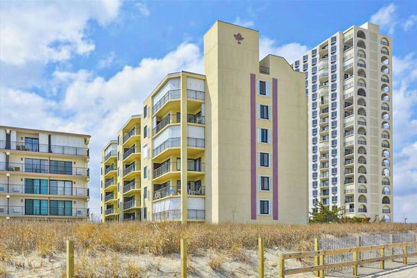 A beachfront hotel with multiple-story buildings, balconies, and a sandy beach area. - Ocean Block Condo with Balcony, Partial Ocean View, Central AC & Washer/Dryer (Ocean City)