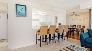 A modern kitchen with white cabinets, a bar area with bar stools, a dining table with chairs, and a blue sofa in a living area. - Ocean Block Condo with Balcony, Partial Ocean View, Central AC & Washer/Dryer (Ocean City)