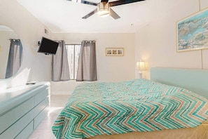 A bedroom with a bed, a ceiling fan, a TV mounted on the wall, and a window with curtains. - Ocean Block Condo with Balcony, Partial Ocean View, Central AC & Washer/Dryer (Ocean City)