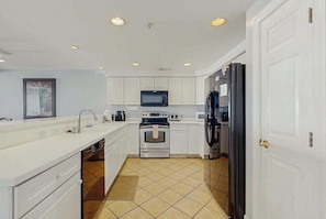 A modern kitchen with white cabinets, a microwave, an oven, a refrigerator, and a sink. - Lovely beachfront condo with ocean view, pool, balcony, fireplace, AC, & W/D (Ocean City)