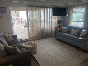 A living room with a sofa, ottoman, and a TV. - Convenient Condo, Updated Waterfront Deck, Free WiFi, Games, Partial A/C, W/D (Ocean City)