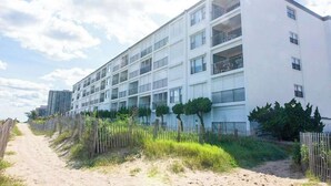 A multi-story building with balconies, a sandy path, and a fence. - Air-Conditioned Condo Steps from the Beach w/ Balcony, WiFi, Washer/Dryer (Ocean City)