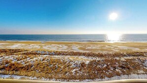A beach with a fence, a clear sky, and the sun reflecting on the water. - Air-Conditioned Condo Steps from the Beach w/ Balcony, WiFi, Washer/Dryer (Ocean City)
