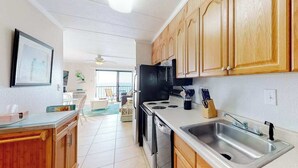 A kitchen with wooden cabinets, a stainless steel sink, a black refrigerator, and a stove. - Air-Conditioned Condo Steps from the Beach w/ Balcony, WiFi, Washer/Dryer (Ocean City)
