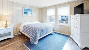 Quarto com cama, penteadeira, mesa de cabeceira, abajur e um quadro na parede.