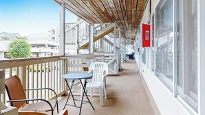 Varanda coberta com cadeiras e mesa de plástico branco, janelas amplas e teto de madeira.