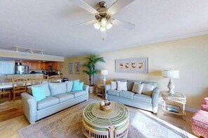 Ein Wohnzimmer mit zwei Sofas, einem Couchtisch, einem Deckenventilator und einer Küche im Hintergrund.
