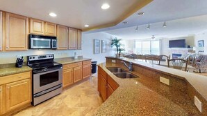 A modern kitchen with granite countertops, stainless steel appliances, wooden cabinets, and a large island with a sink. - Incredible Beachfront Condo w/Private Balcony, Fireplace, A/C, & Shared Pool (Ocean City)