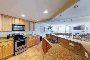 Eine moderne Küche mit Granit-Arbeitsplatten, Edelstahlgeräten, Holzschränken und einer großen Kochinsel mit Spüle.