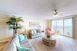A living room with a sofa, a round coffee table, a ceiling fan, and a large window with a view. - Incredible Beachfront Condo w/Private Balcony, Fireplace, A/C, & Shared Pool (Ocean City)