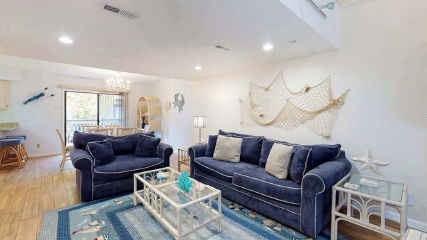 A living room with two dark blue sofas, a glass coffee table, a patterned rug, and a decorative wall hanging. - Marlin Cove 405 (Ocean City)