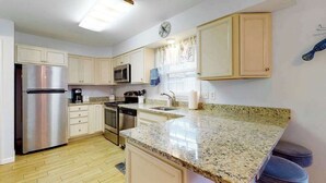 A kitchen with white cabinets, stainless steel appliances, a granite countertop, and a clock on the wall. - Marlin Cove 405 (Ocean City)