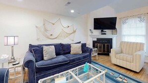 A living room with a blue sofa, a white armchair, a TV, and a fireplace. - Marlin Cove 405 (Ocean City)