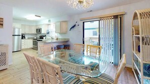 A modern kitchen with white cabinets, a stainless steel refrigerator, and a dining area with a glass table and wicker chairs. - Marlin Cove 405 (Ocean City)