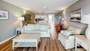 A living room with a sofa, a coffee table, a dining area, and a kitchen in the background. - Beachfront Condo w/Private Balcony, Beach Views, Washer/Dryer, Central A/C (Ocean City)