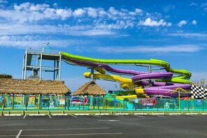 A water park with a multi-lane water slide, a thatched-roof structure, and a fenced entrance area. - Ocean Club 4007 (Ocean City)
