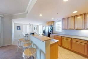 A modern kitchen with a central island, wooden cabinets, and a dining area with stools. - Terrific Beach Condo w/Spacious Balcony, W/D, Shared Pool, Fitness Center, WiFi (Ocean City)