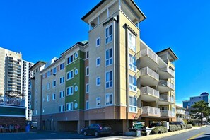 A multi-story residential building with balconies, a parking area, and a street view. - Terrific Beach Condo w/Spacious Balcony, W/D, Shared Pool, Fitness Center, WiFi (Ocean City)