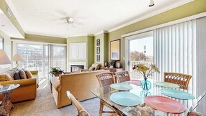Ein großzügiges Wohnzimmer mit einer Couch, Sesseln, einem Glastisch und einem Balkon mit großen Fenstern.