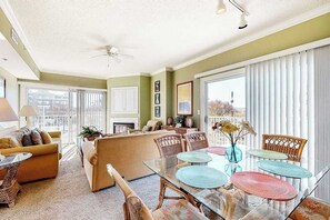 Ein großzügiges Wohnzimmer mit einer Couch, Sesseln, einem Glastisch und einem Balkon mit großen Fenstern.