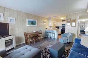 Ein Wohnzimmer mit Sofa, Fernseher, Essbereich mit Stühlen, Küche mit Arbeitsfläche und einer Treppe.