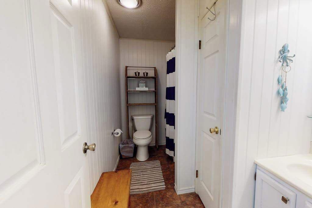 Een smalle gang die leidt naar een badkamer met een toilet, planken en een klein vloerkleed.